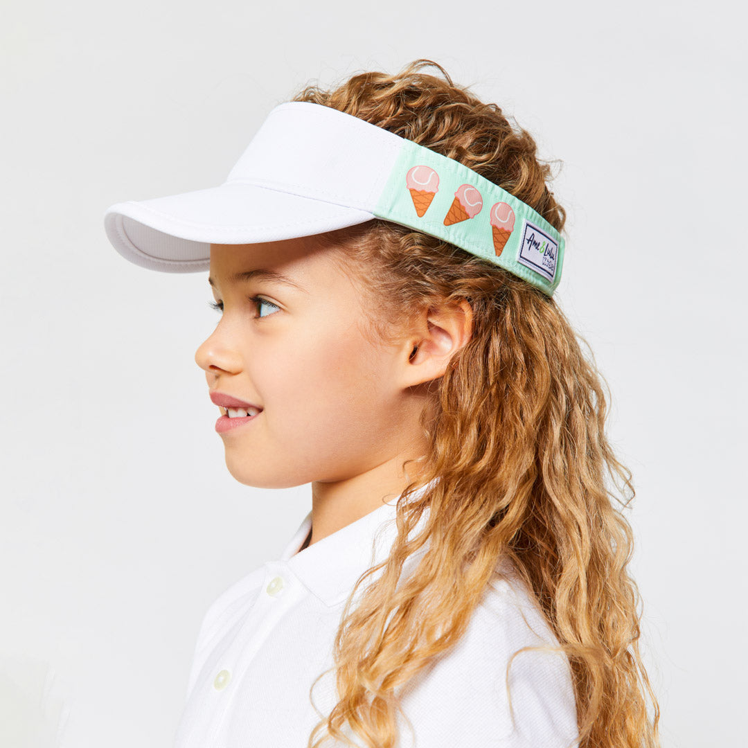 Little girl wearing light green kids visor with pink tennis ball ice creams on the sides.