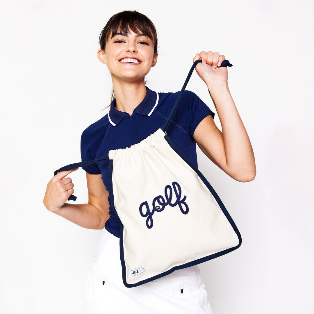 woman holding tan canvas drawstring shoe bag with the word golf embroidered on front in navy cursive