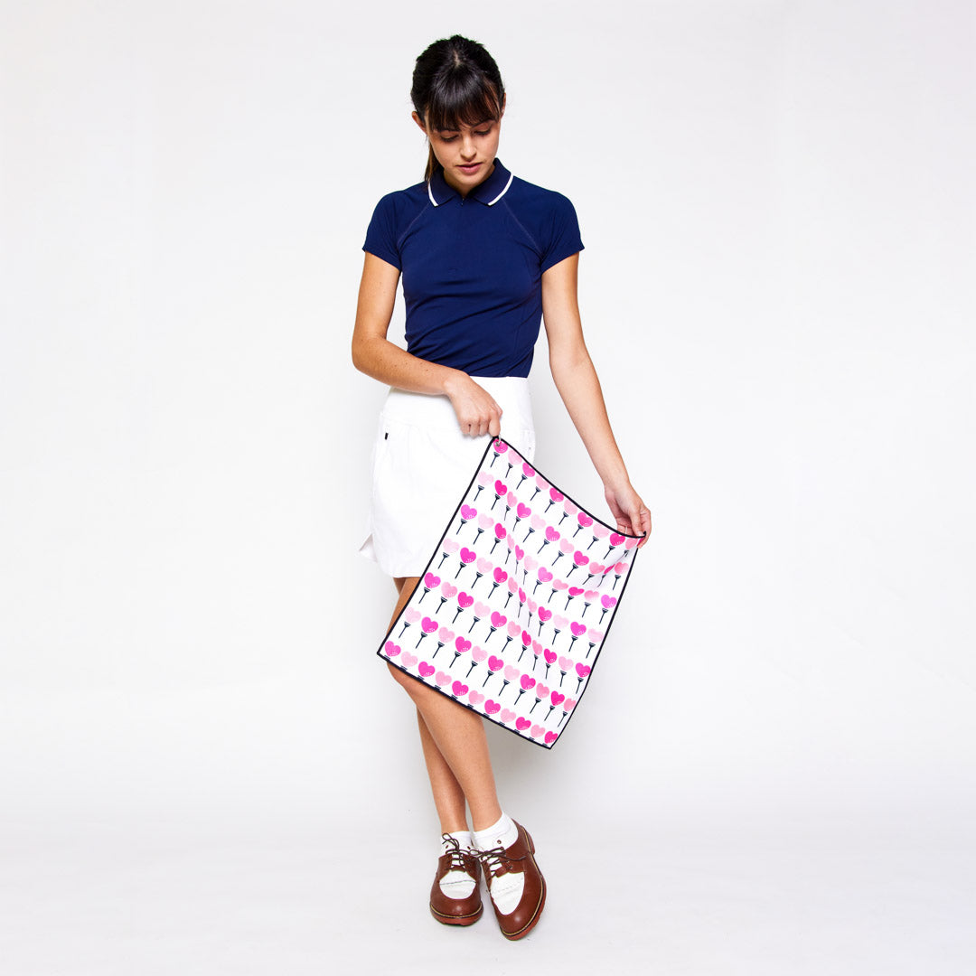 woman holds small white towel with hot pink and pink heart shaped golf balls and tee