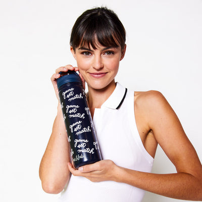 Woman holds Navy water bottle with game set match text repeating print on bottle.