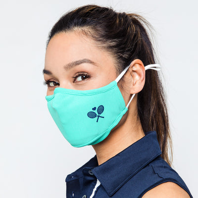 woman wears teal face mask with navy crossed racquets printed on one side