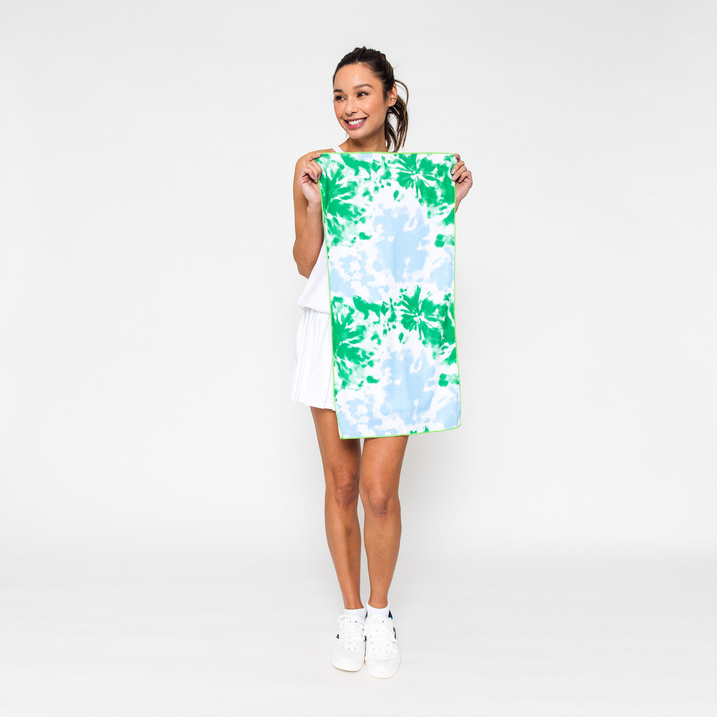 Woman holds rectangular towel printed with green and blue tie dye pattern.