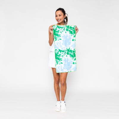 Woman holds rectangular towel printed with green and blue tie dye pattern.
