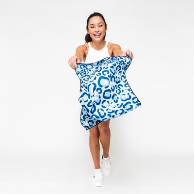 Woman waves rectangular towel with blue leopard and repeating white tennis racquets pattern.