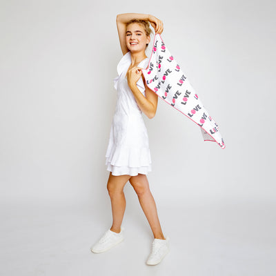 Woman waves around White rectangular towel with repeating pattern of the word love with the letter o is a hot pink tennis ball