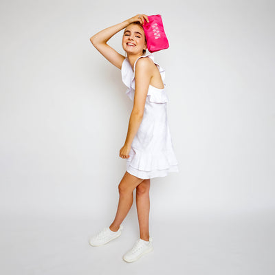 Woman holds small everyday pouch with top zipper. Pouch is pink with light pink racquets printed across the front.