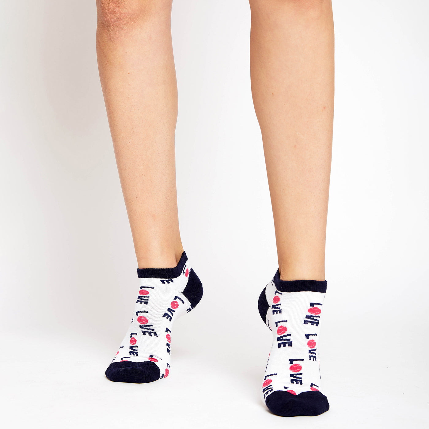 woman wears a pair of white socks with navy heels and toes. The word love in navy with a pink tennis ball for the letter o are printed around the socks