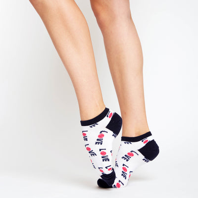 Woman wears a pair of white socks with navy heels and toes. The word love in navy with a pink tennis ball for the letter o are printed around the socks