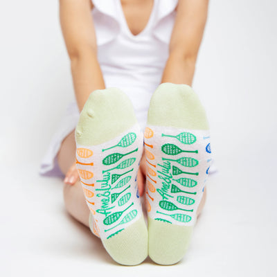 woman wears a Pair of white socks with lime green heels and toes. Rainbow racquets are printed around the socks.