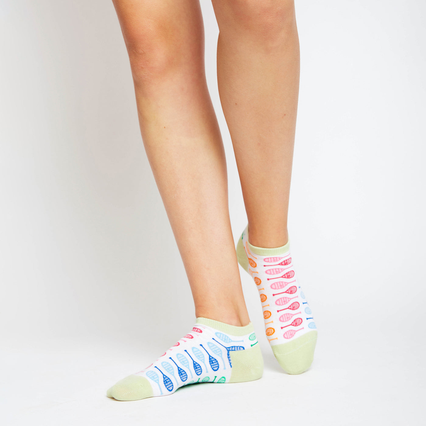 Woman wears a Pair of white socks with lime green heels and toes. Rainbow racquets are printed around the socks.