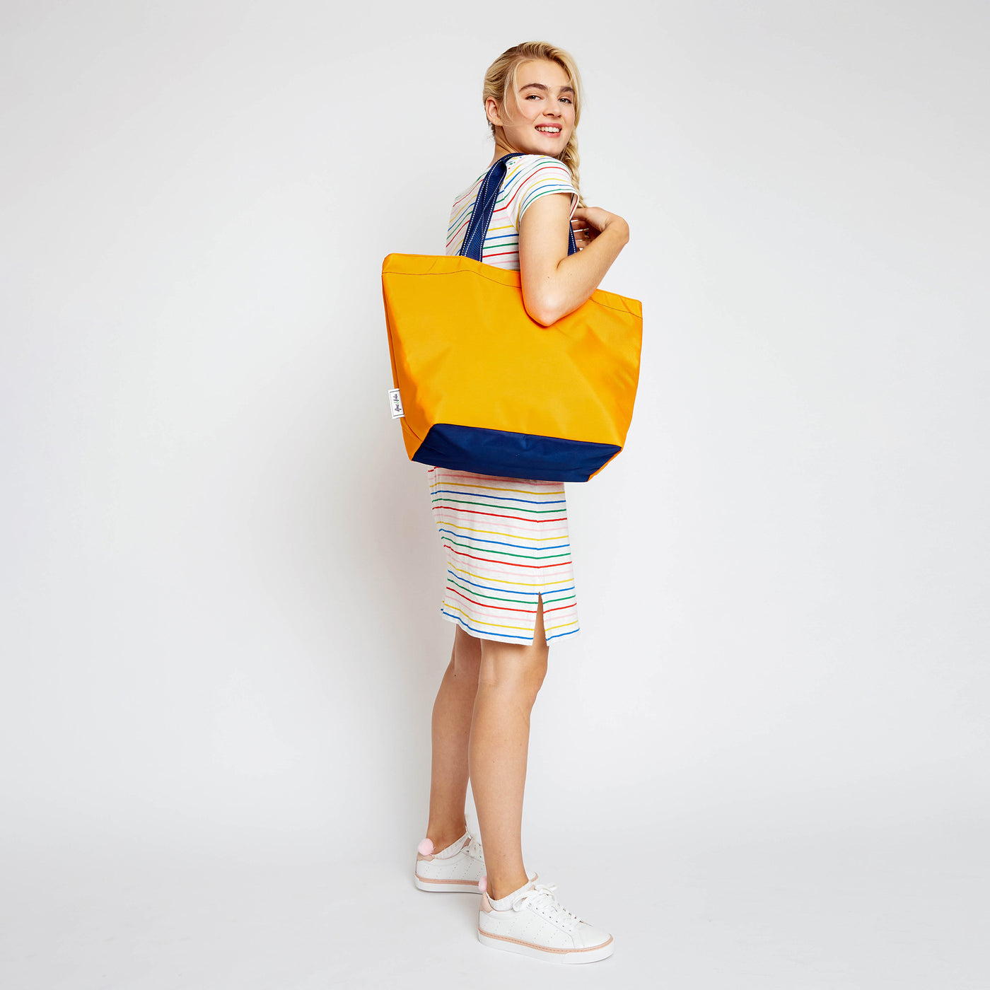 woman holding orange nylon tote bag with navy straps on her shoulder