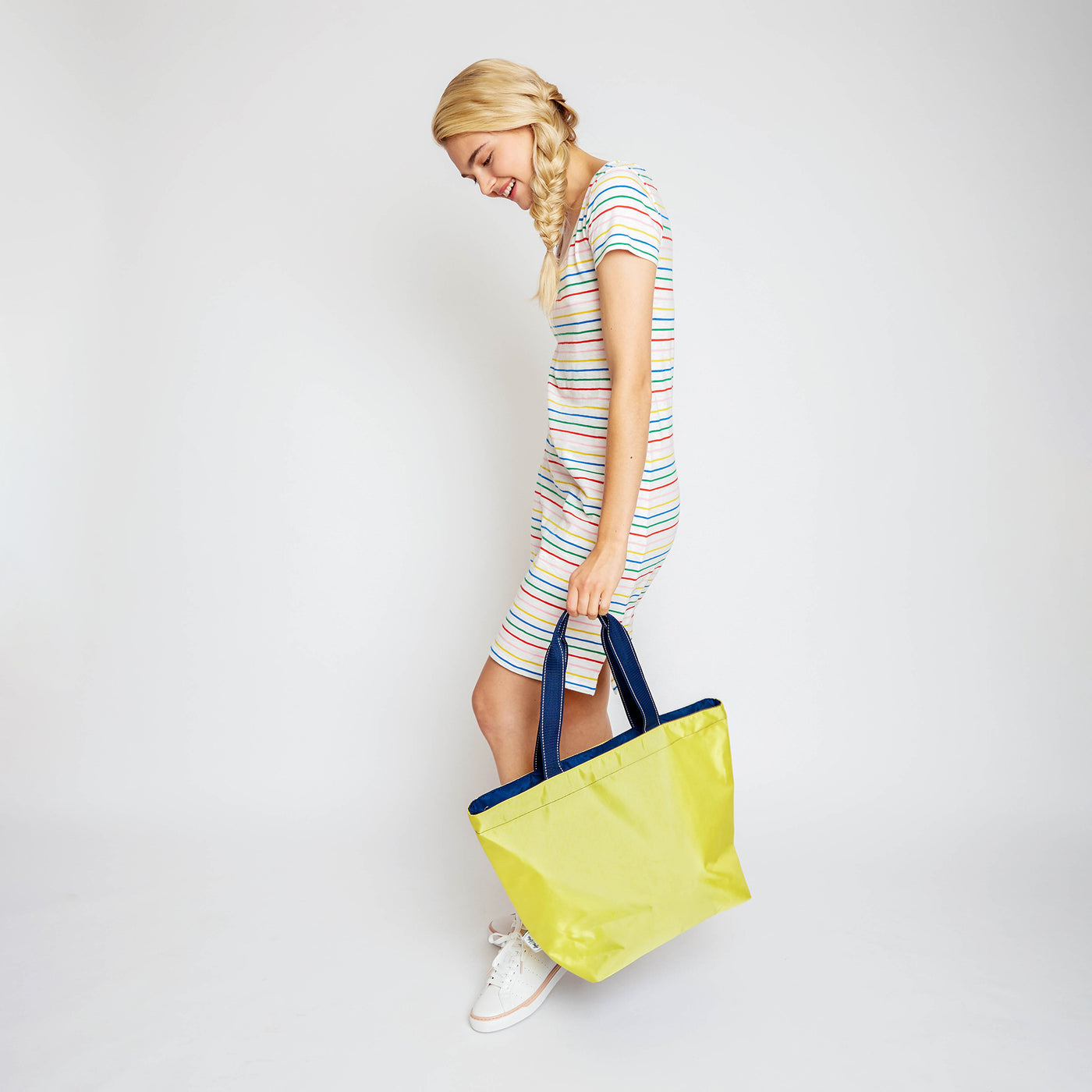 woman holding yellow nylon tote bag with navy straps by her feet