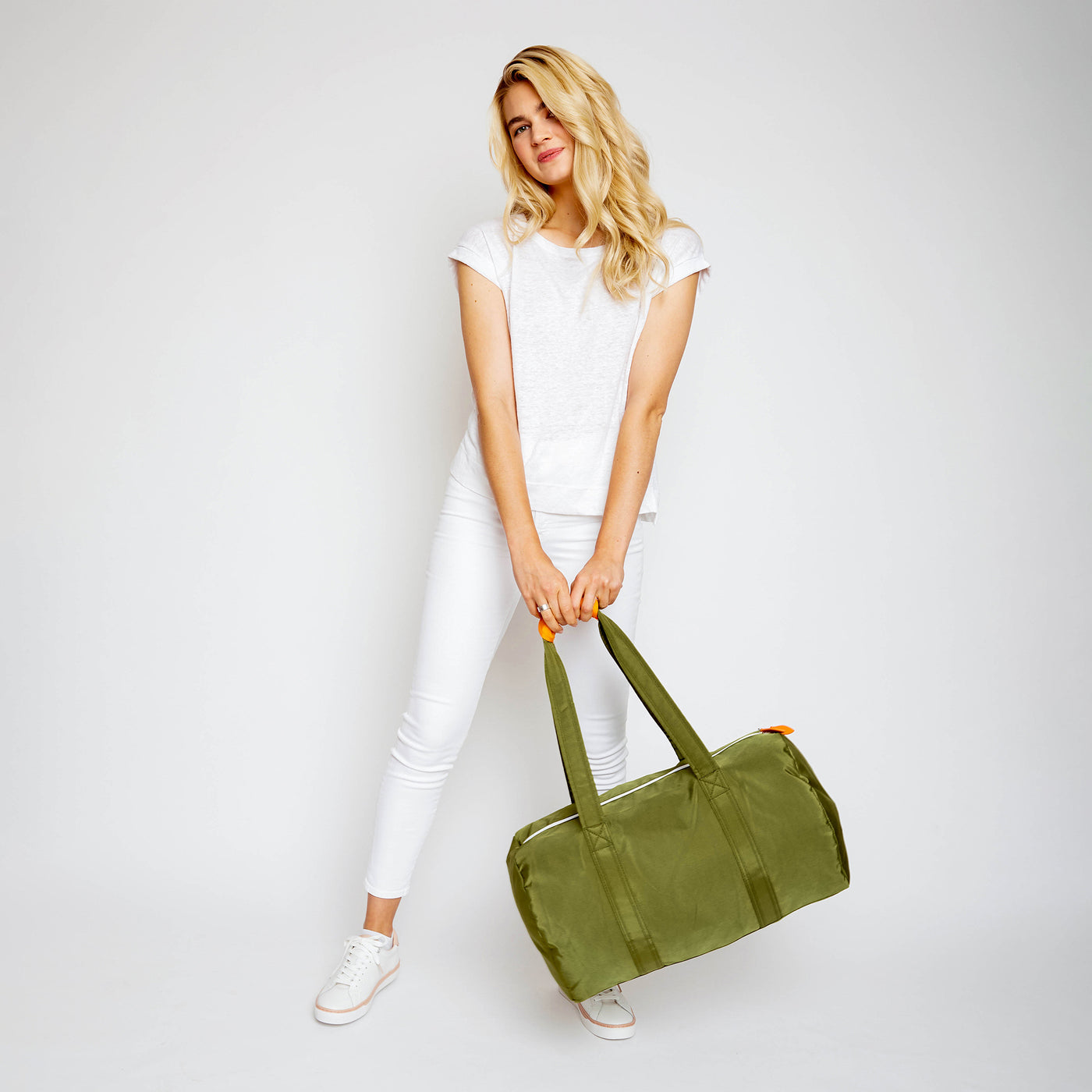 woman holding army green duffel with orange cap on the straps