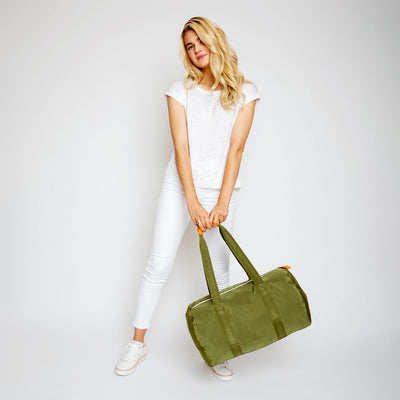 woman holding army green duffel with orange cap on the straps