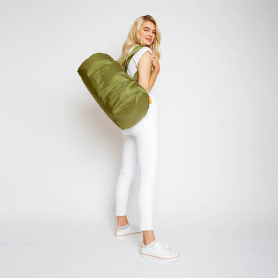 woman holding army green duffel with orange cap on the straps over her shoulder