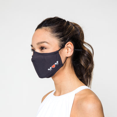 woman wears charcoal grey face mask with white tennis racquets and red heart printed on one sid