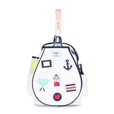 Front view of white kids tennis backpack with removeable patches. Patches are nautical themes with anchor, lighthouse, sailing flags, crossed racquets and heart.