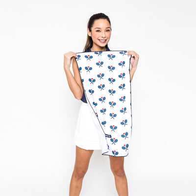 Woman holds up White rectangular towel with repeating navy crossed racquets and red hearts.
