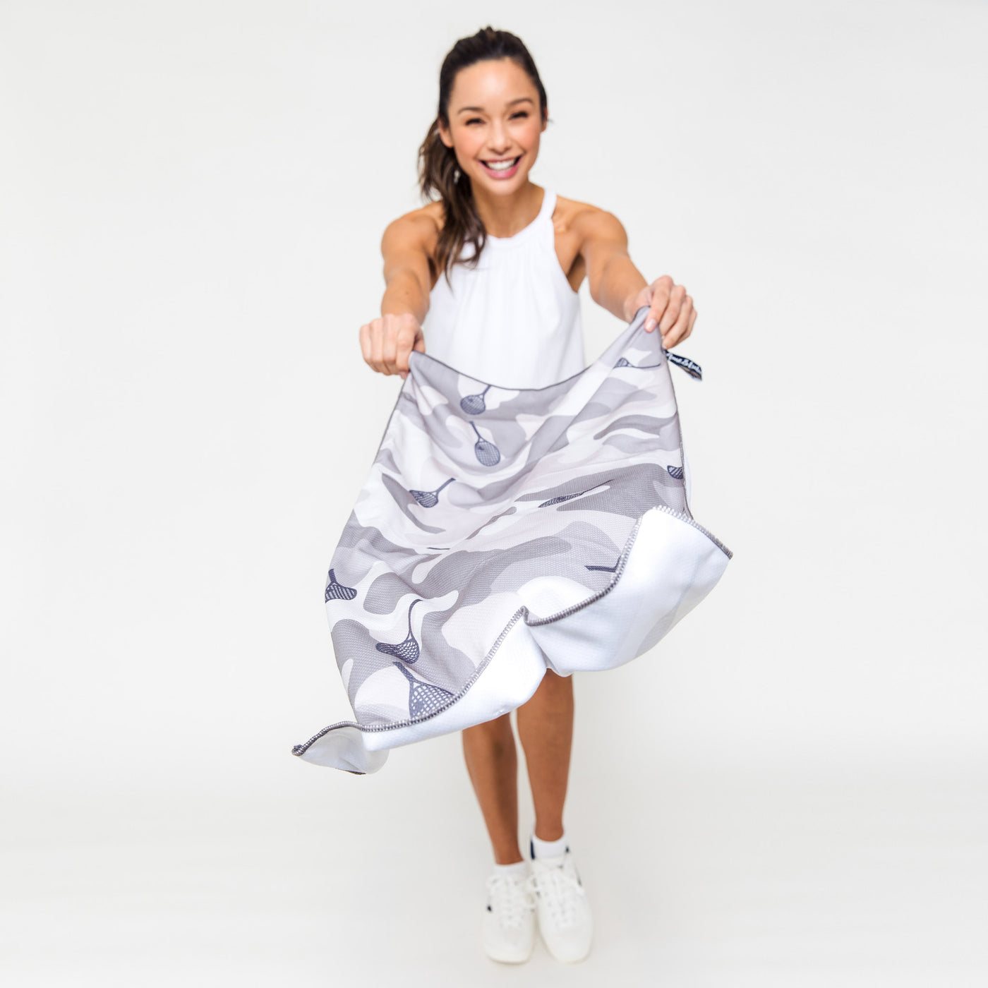 Woman waves rectangular towel printed with grey camo and repeating grey tennis racquet pattern.