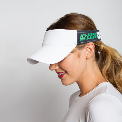 Woman on white background wears the racquets visor. Front of visor is white and the sides are navy with green racquets