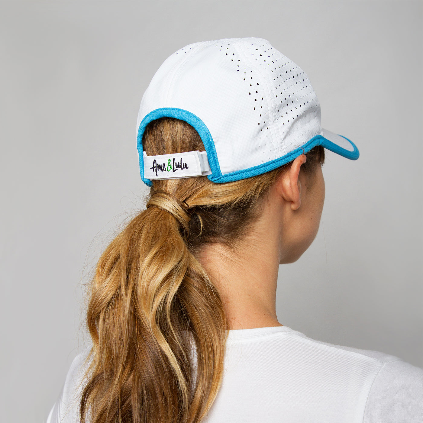back view of woman wearing white sport hat with blue trim.