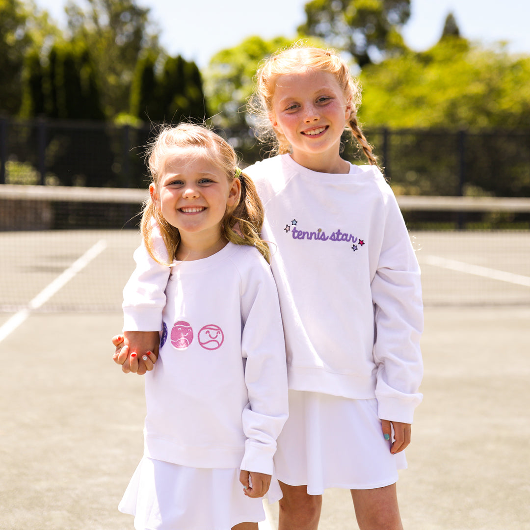 two little girls wearing white kids sweatshirt with the word tennis star embroidered in purple cursive font on front