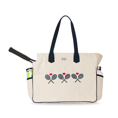 Front view of love all court bag. Large canvas tennis tote with tennis racquet inside and crossed navy racquets and red hearts printed across the front of bag.