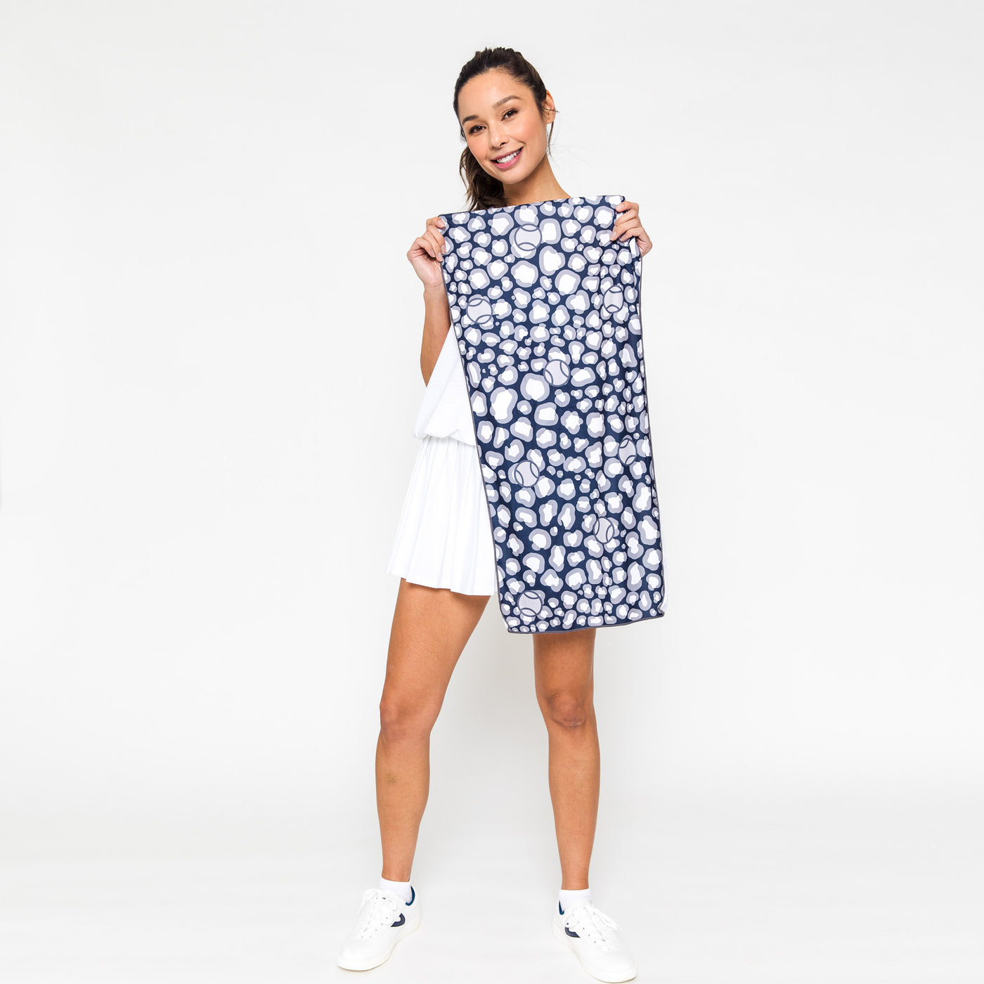 woman holds up Rectangular towel with navy and grey repeating leopard pattern with tennis balls icons printed over the leopard.
