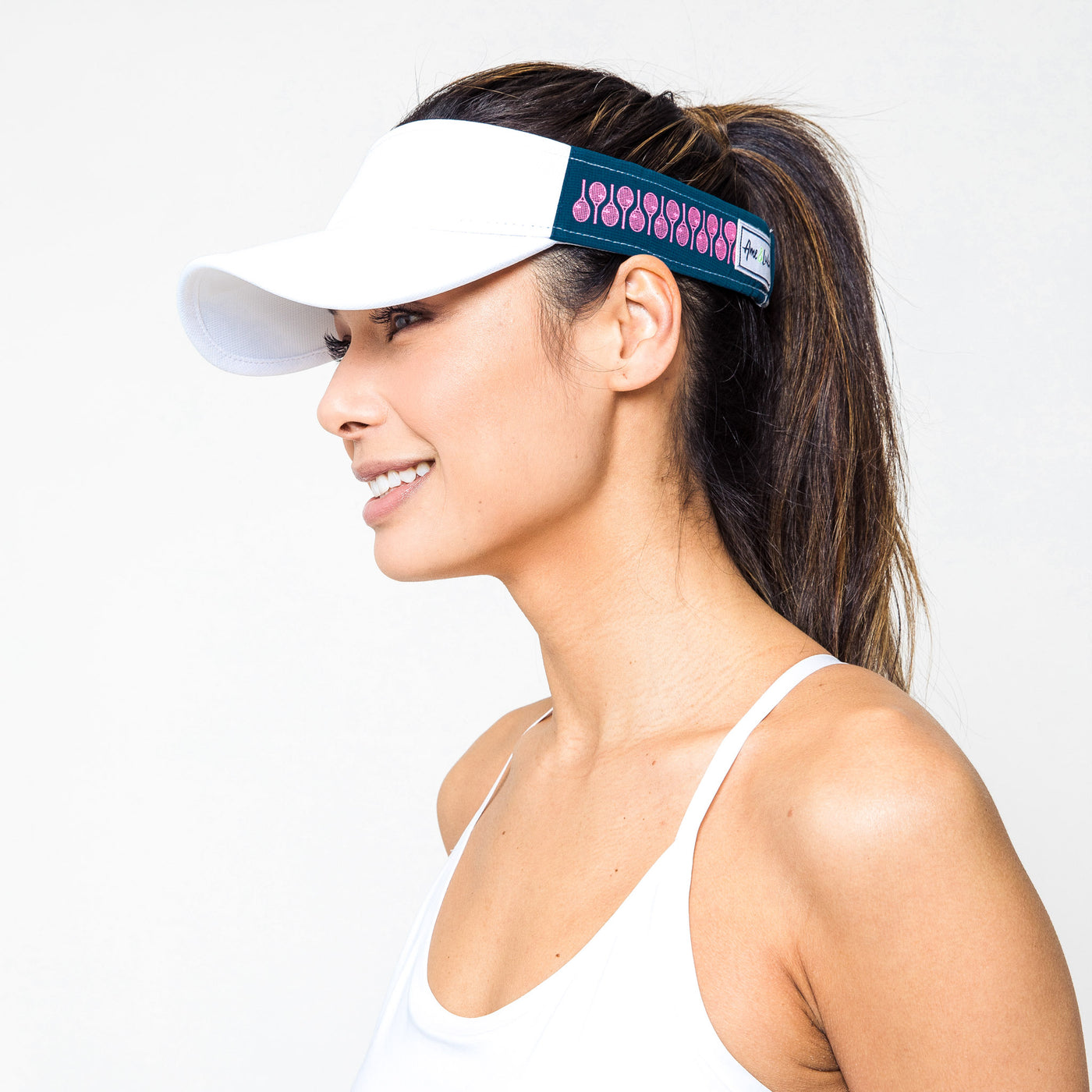 Woman on white background wears Navy Pink Racquets Head in the game visor. Front of visor is white and the sides are navy with hot pink racquets printed on the navy.