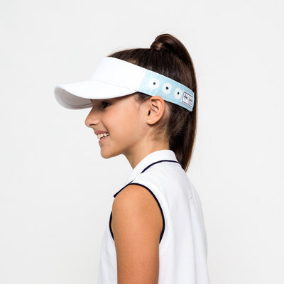 Little girl wearing light blue kids visor with white daisies and navy tennis balls printed on sides.
