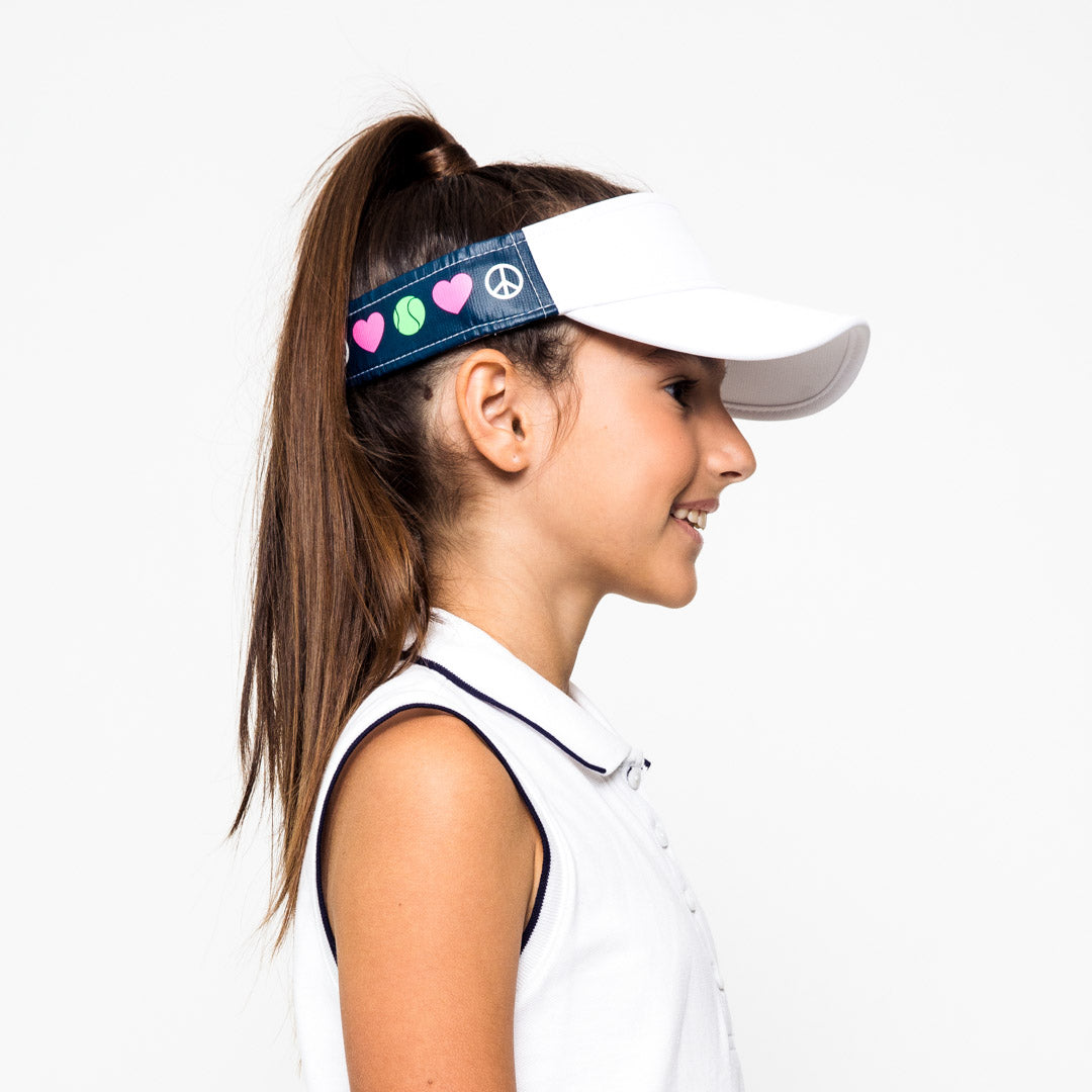 Little girl wearing navy kids visor with white peace sign, pink heart and green tennis ball printed on sides