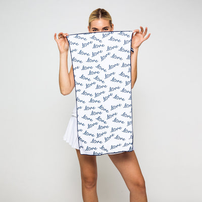 Woman holds in front of her face a rectangular white towel with repeating pattern of the word love in a cursive font