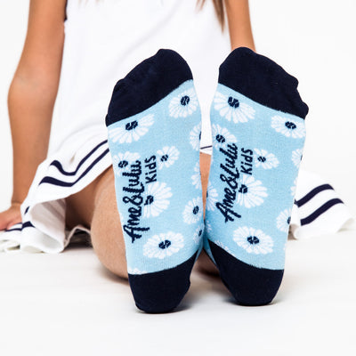 girl wearing pair of light blue kids socks with navy heel and toes, and white daisies stitched on socks