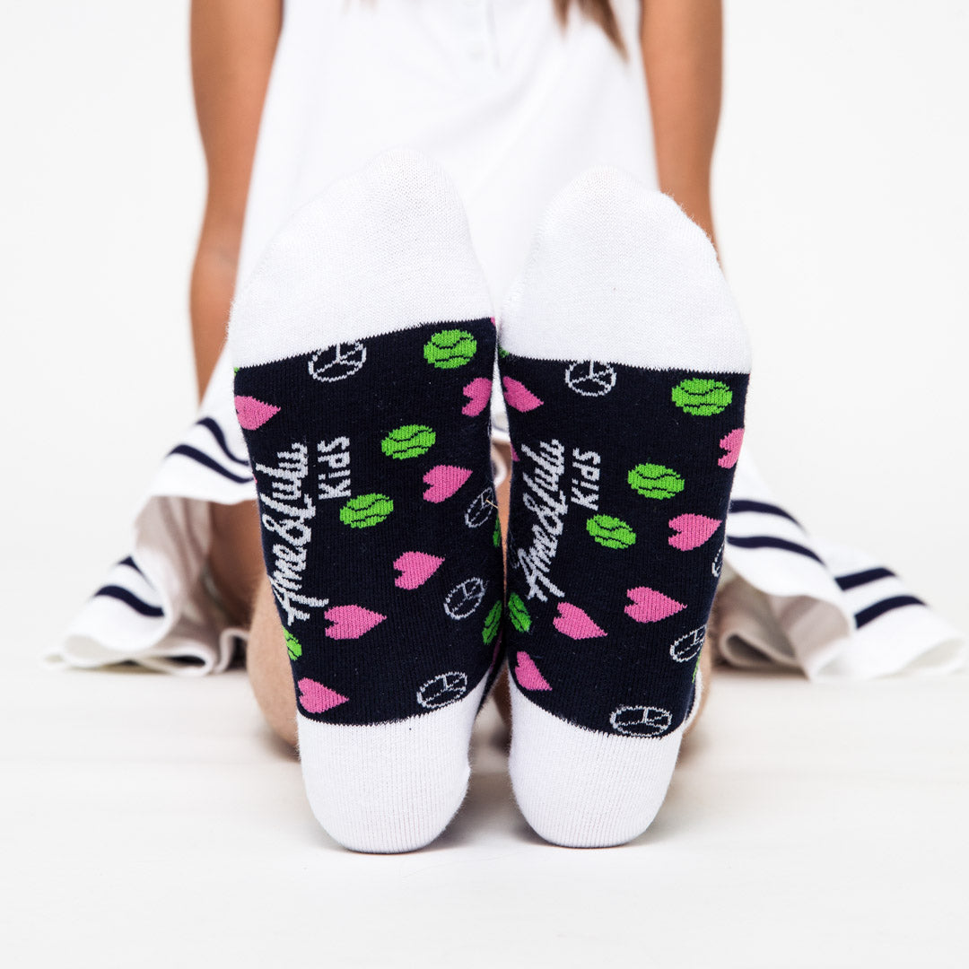 girl wearing pair of navy kids socks with white heel and toes, and peace signs heart and tennis balls stitched on to sock