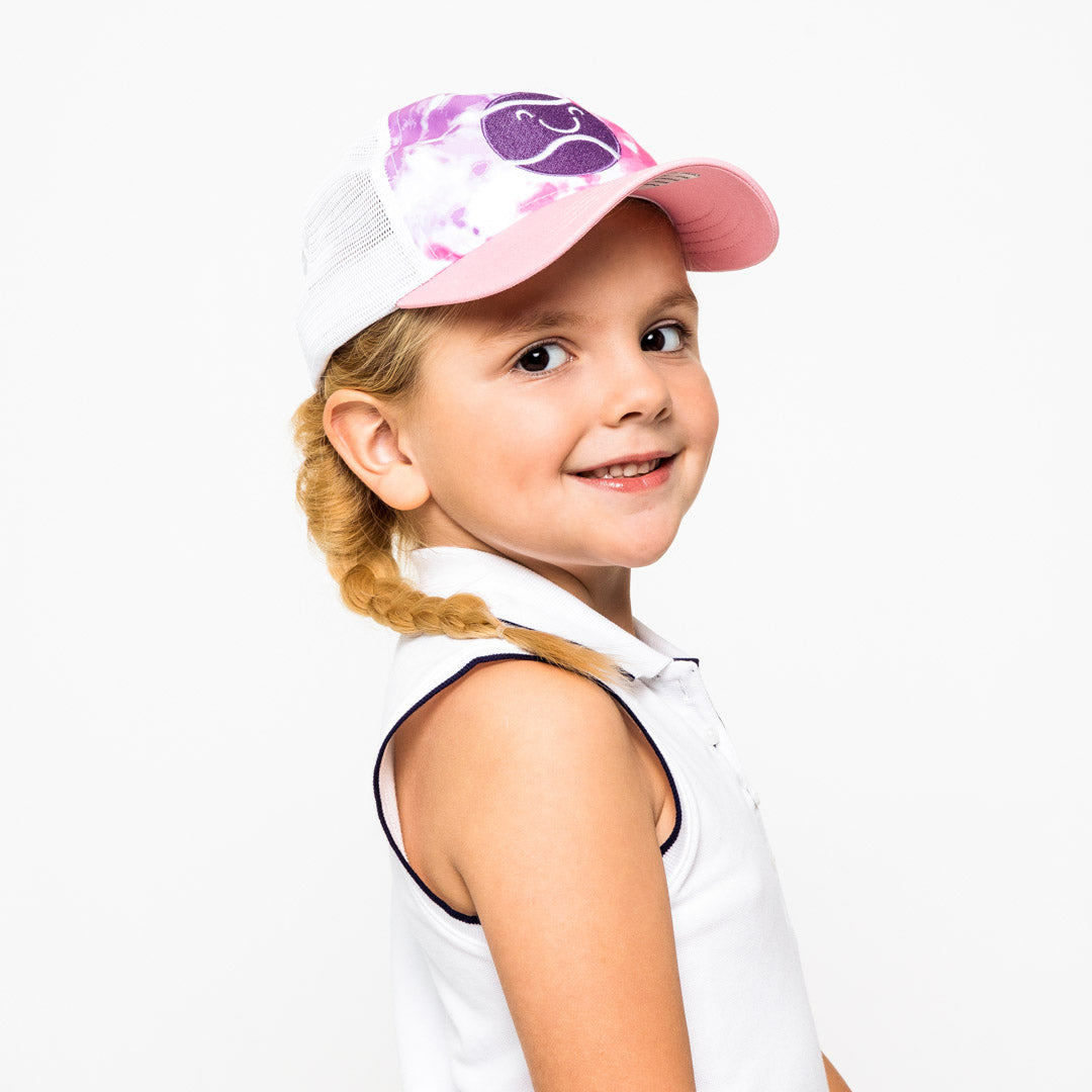 Little girl wearing pink purple and white tie dye kids trucker hat with purple smiling tennis ball embroidered on front