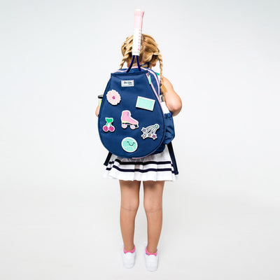 Little girl stands wearing navy tennis backpack with different tennis themed patches.