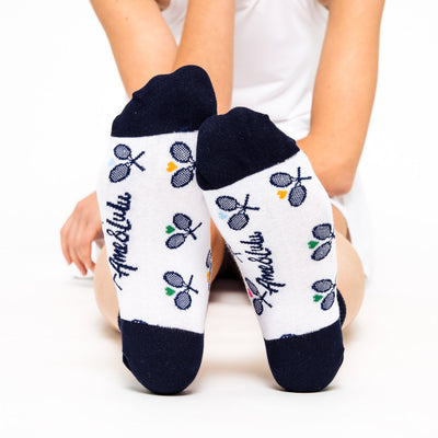woman wears a pair of white socks with navy heels and toes, and navy crossed racquets and rainbow hearts pattern on socks