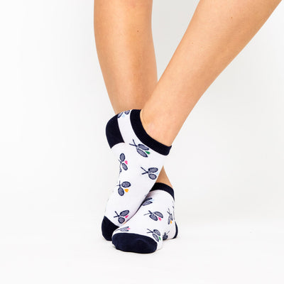woman wears a pair of white socks with navy heels and toes, and navy crossed racquets and rainbow hearts pattern on socks