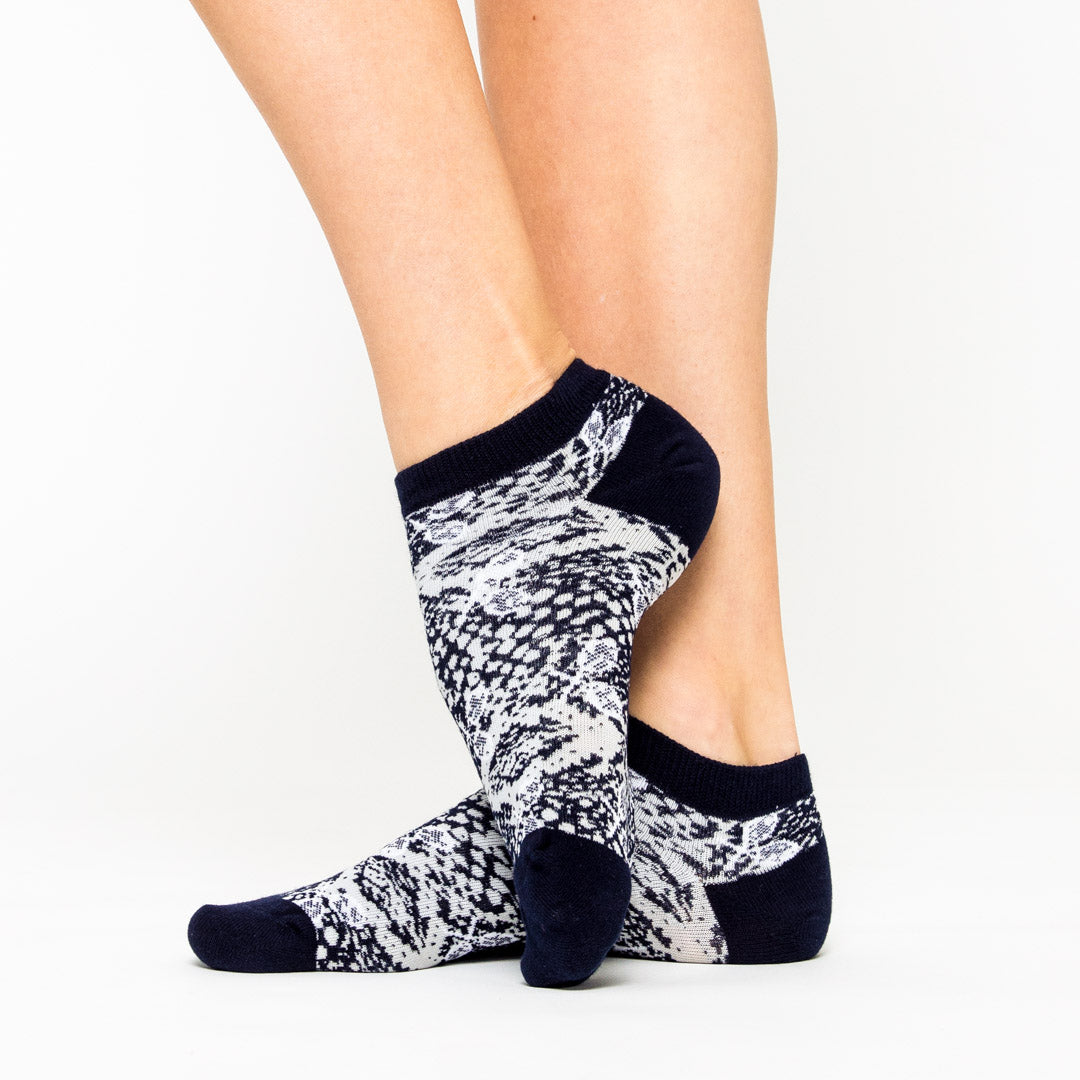 woman wears a pair of grey socks with navy and grey snakeskin and white tennis racquets pattern