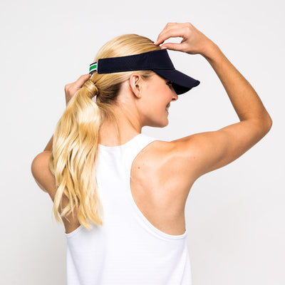 Woman wears navy visor with white, navy and green striped adjustable strap on the back.