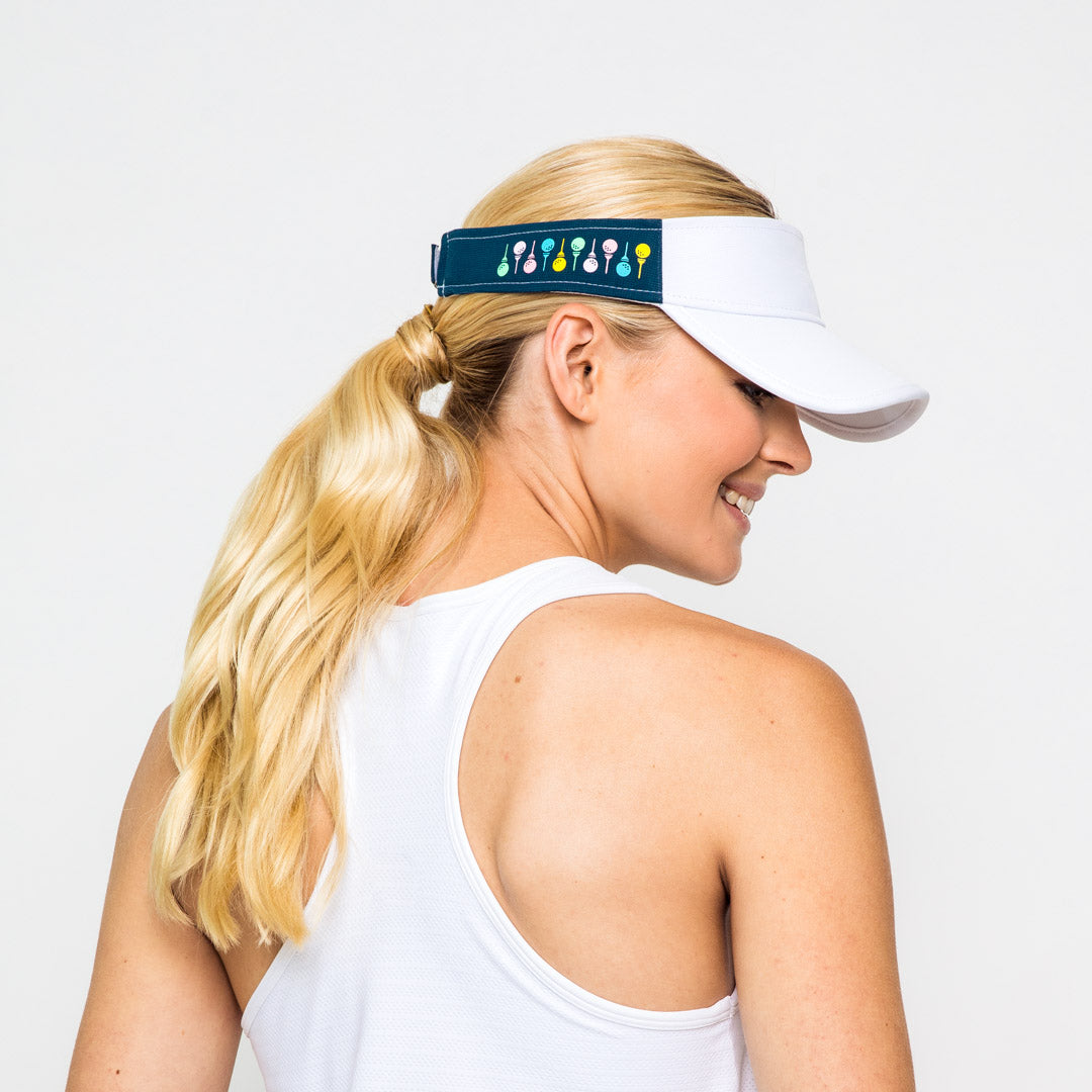 woman wears navy womens visor with pastel rainbow golf balls and tee printed on sides.