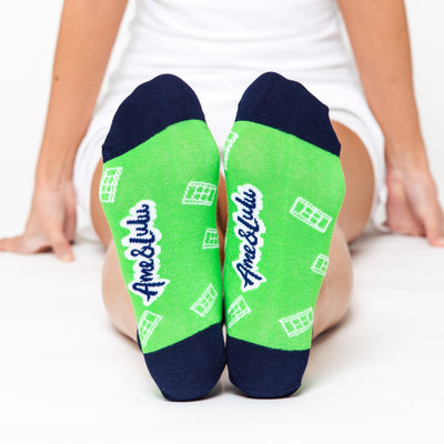 woman wears a pair of green socks with navy heels and toes. White tennis courts are a repeat pattern on the socks