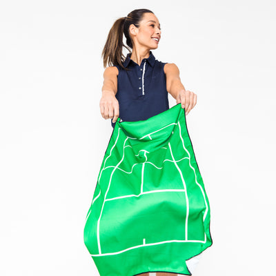 Woman waves arounds Green rectangular towel with navy trim and white tennis court printed on front.