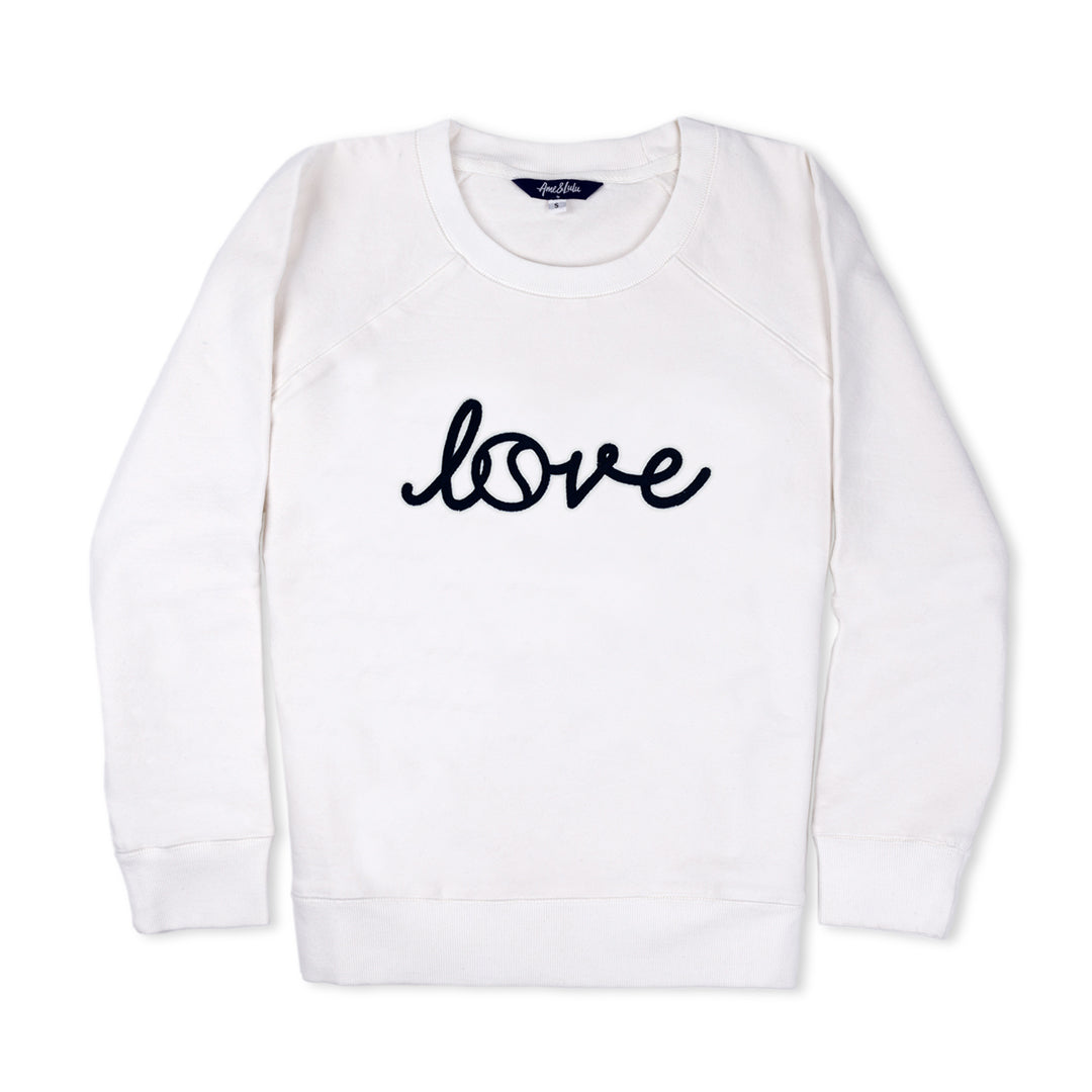 White sweatshirt lays flat with cursive font that reads love across the front in navy