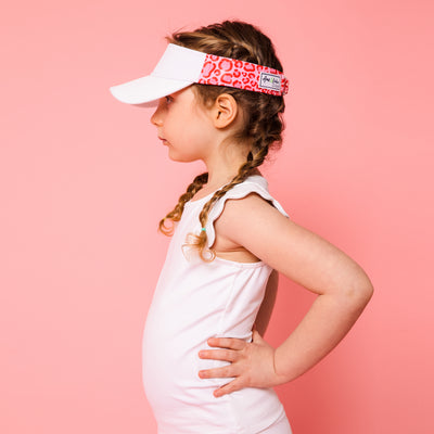 Little girl standing on pink background wearing hot pink and red leopard pattern kids visor.