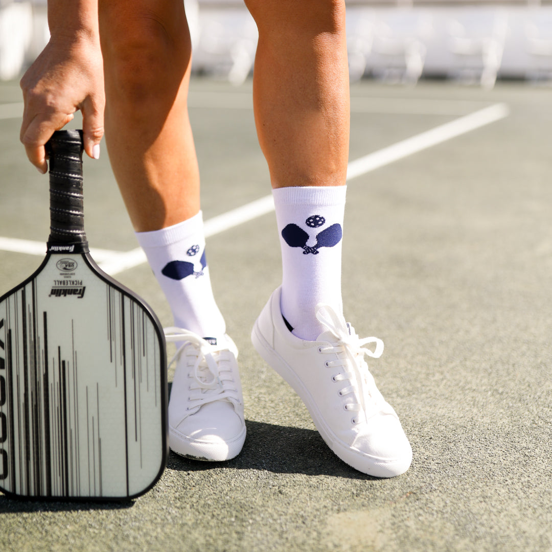 woman standing on a pickleball court wearing white crew socks and holding a pickleball paddle
