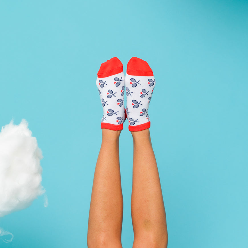 Woman sticks feet up in air on a blue background wearing white socks with red trim and navy racuqets