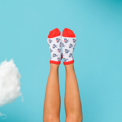 Woman sticks feet up in air on a blue background wearing white socks with red trim and navy racuqets