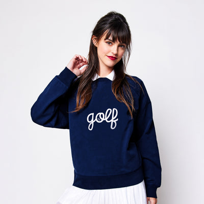 woman wears navy sweatshirt with the word golf embroidered on the front in white cursive text